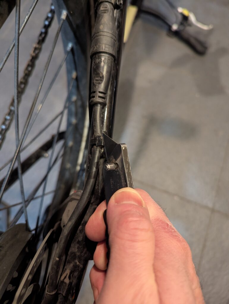 A hand holds a utility knife against a cable tie wrapped around the power cable for the rear wheel motor