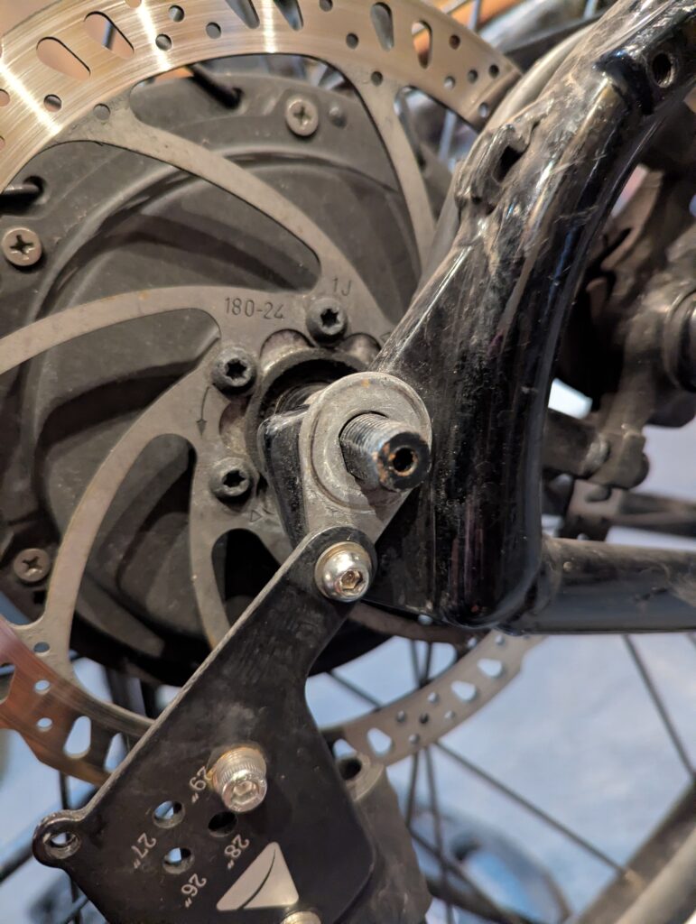 A close up of the bike showing a metal bracket that holds the rack that is also holding the wheel skewer in place