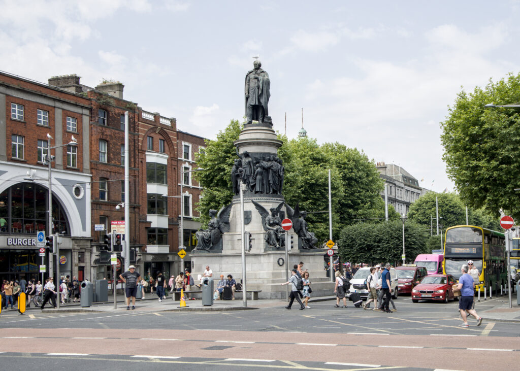 A statue of a man on top of a large pedestal. People sit at the base. He has a seagull sitting on his head